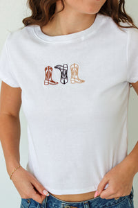 White t-shirt with cowboy boot designs worn by a person on a plain background