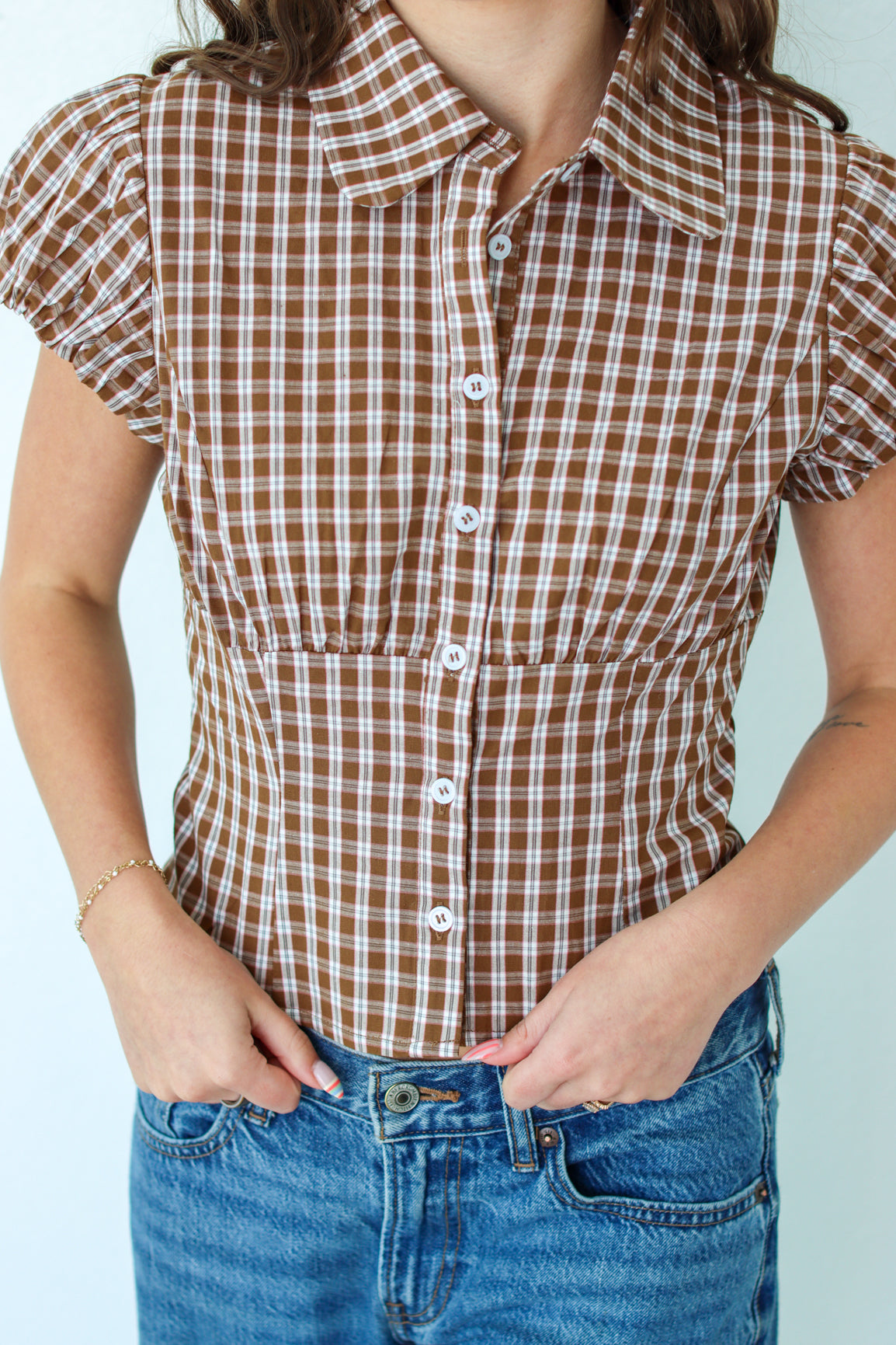 Woman wearing a brown checkered shirt and jeans against a white background