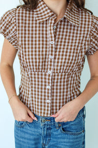 Woman wearing a brown checkered shirt and jeans against a white background