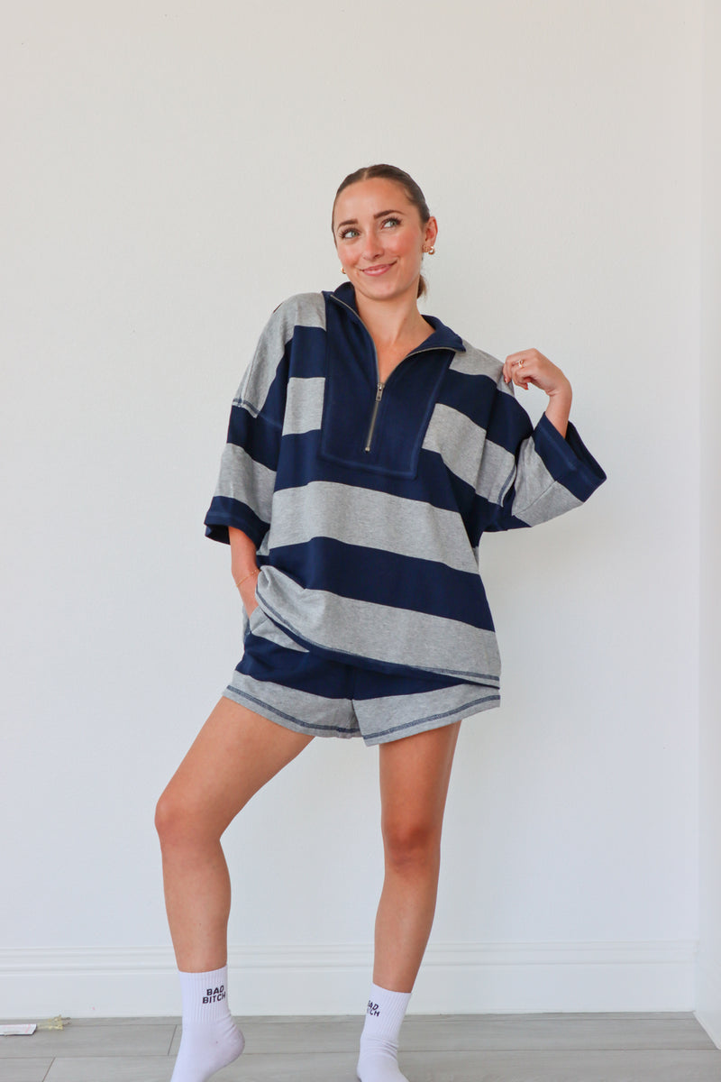 Woman wearing a blue and gray striped sweater and shorts set against a white background