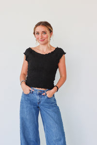 Woman wearing a black top and blue jeans against a plain background