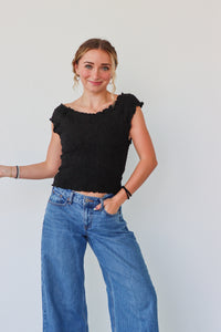 Woman wearing a black top and blue jeans against a plain background