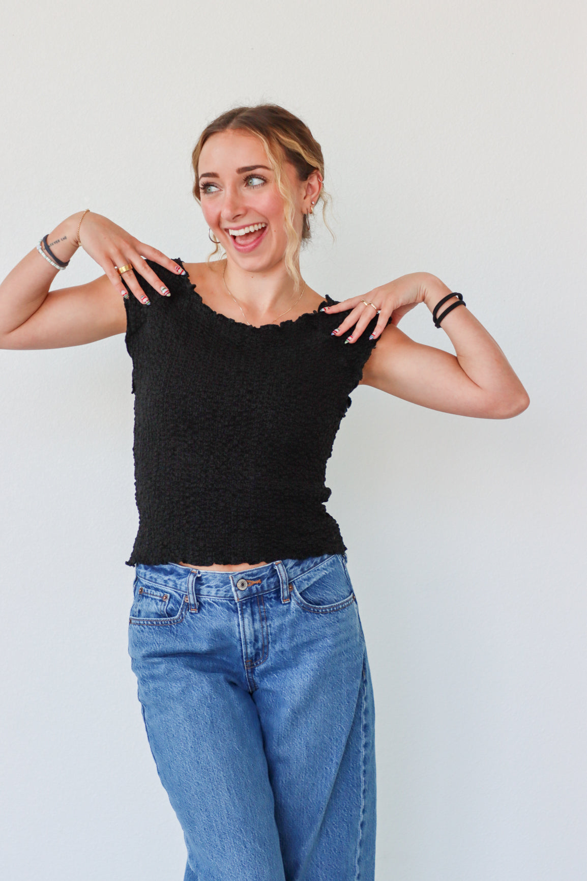 Woman wearing a black top and blue jeans against a white background