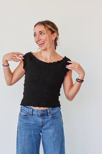 Woman wearing a black top and blue jeans against a plain background
