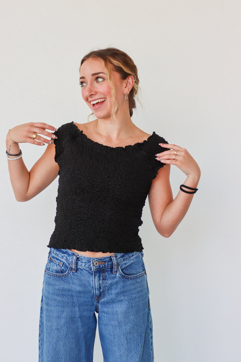 Woman wearing a black top and blue jeans against a plain background