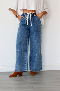 Person wearing blue wide-leg jeans with a white top against a plain background