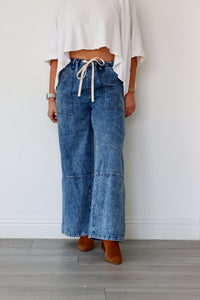 Person wearing blue wide-leg jeans and a white top against a plain background