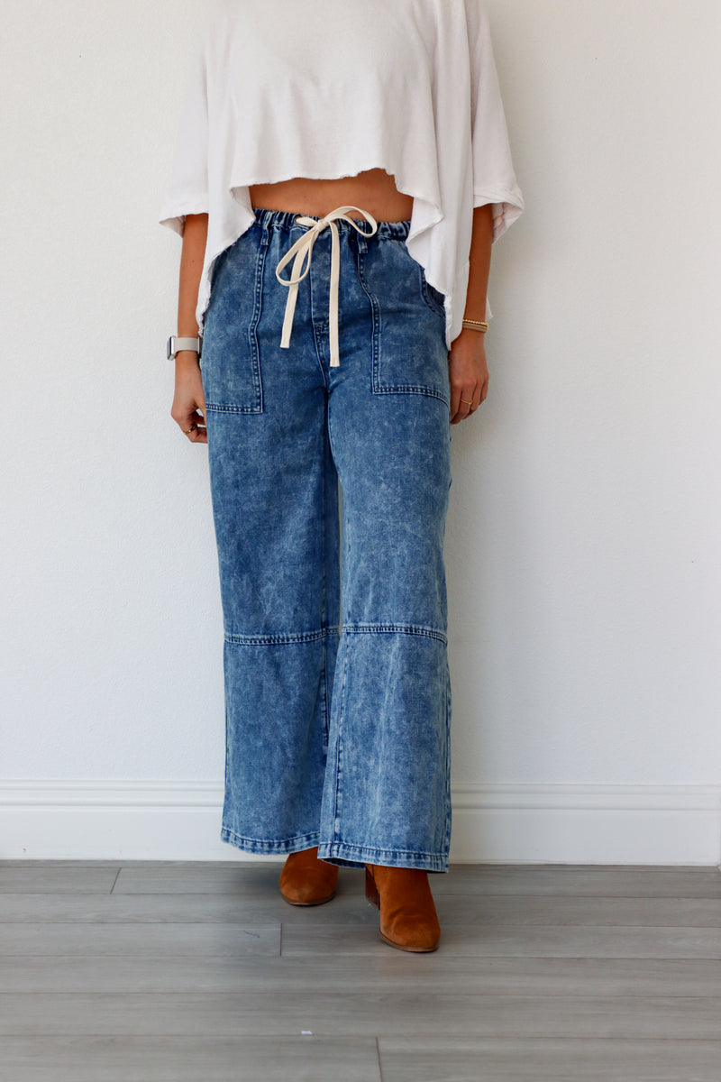 Person wearing blue wide-leg jeans and a white top against a plain background