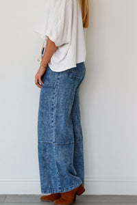 Person wearing a white top and blue wide-leg jeans against a plain background