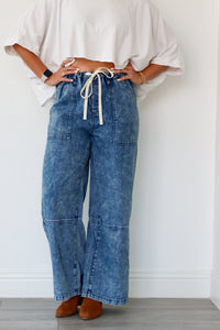 Person wearing blue denim wide-leg pants with a white top against a plain background