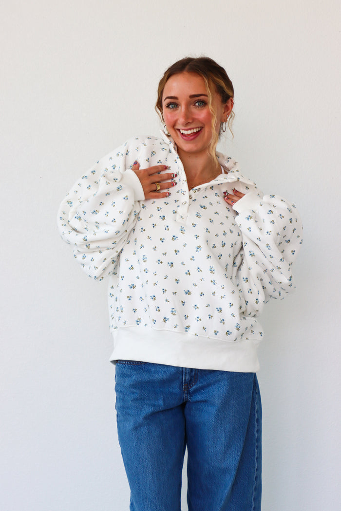 Woman wearing a white floral blouse and blue jeans against a white background