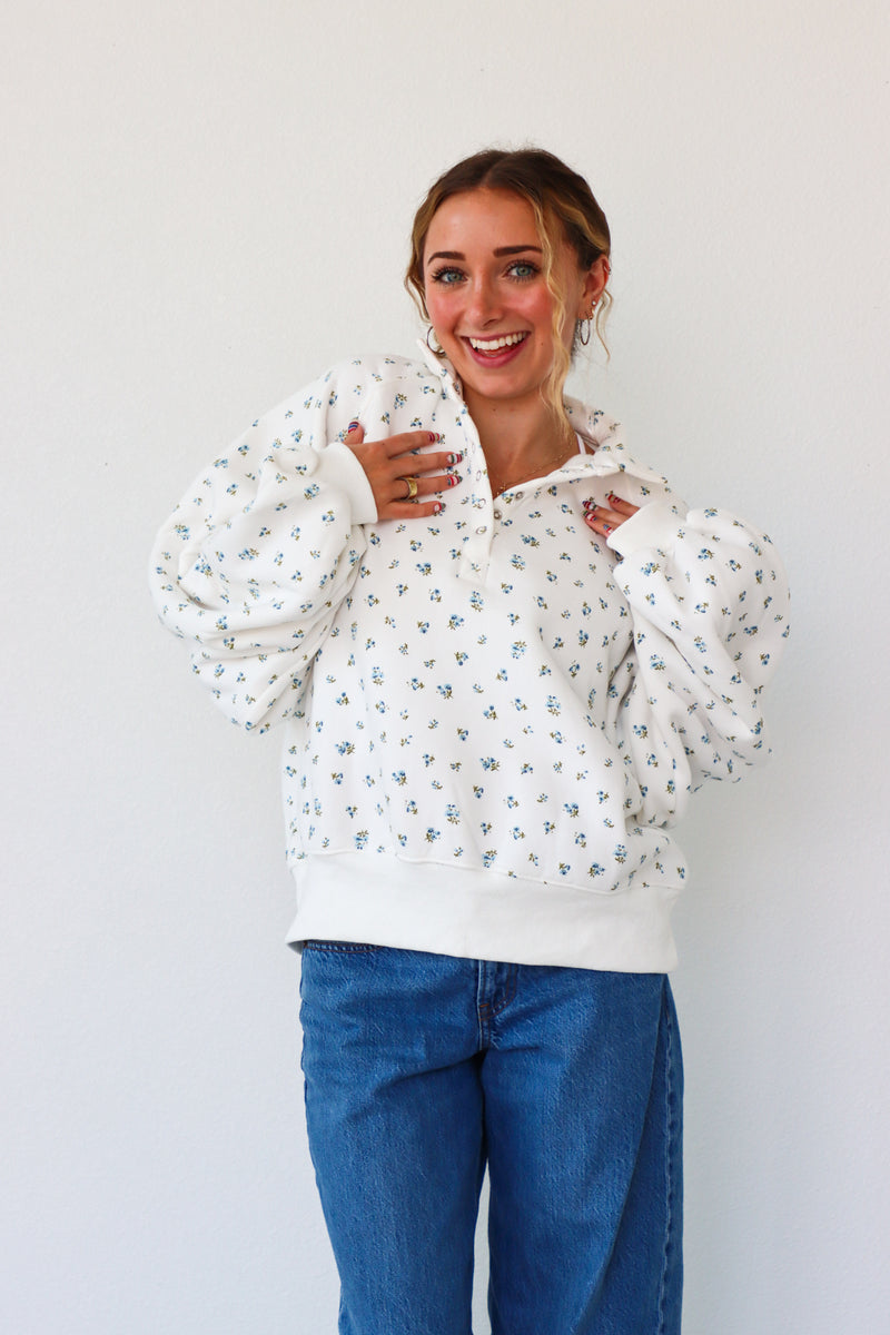 Woman wearing a white floral blouse and blue jeans against a white background