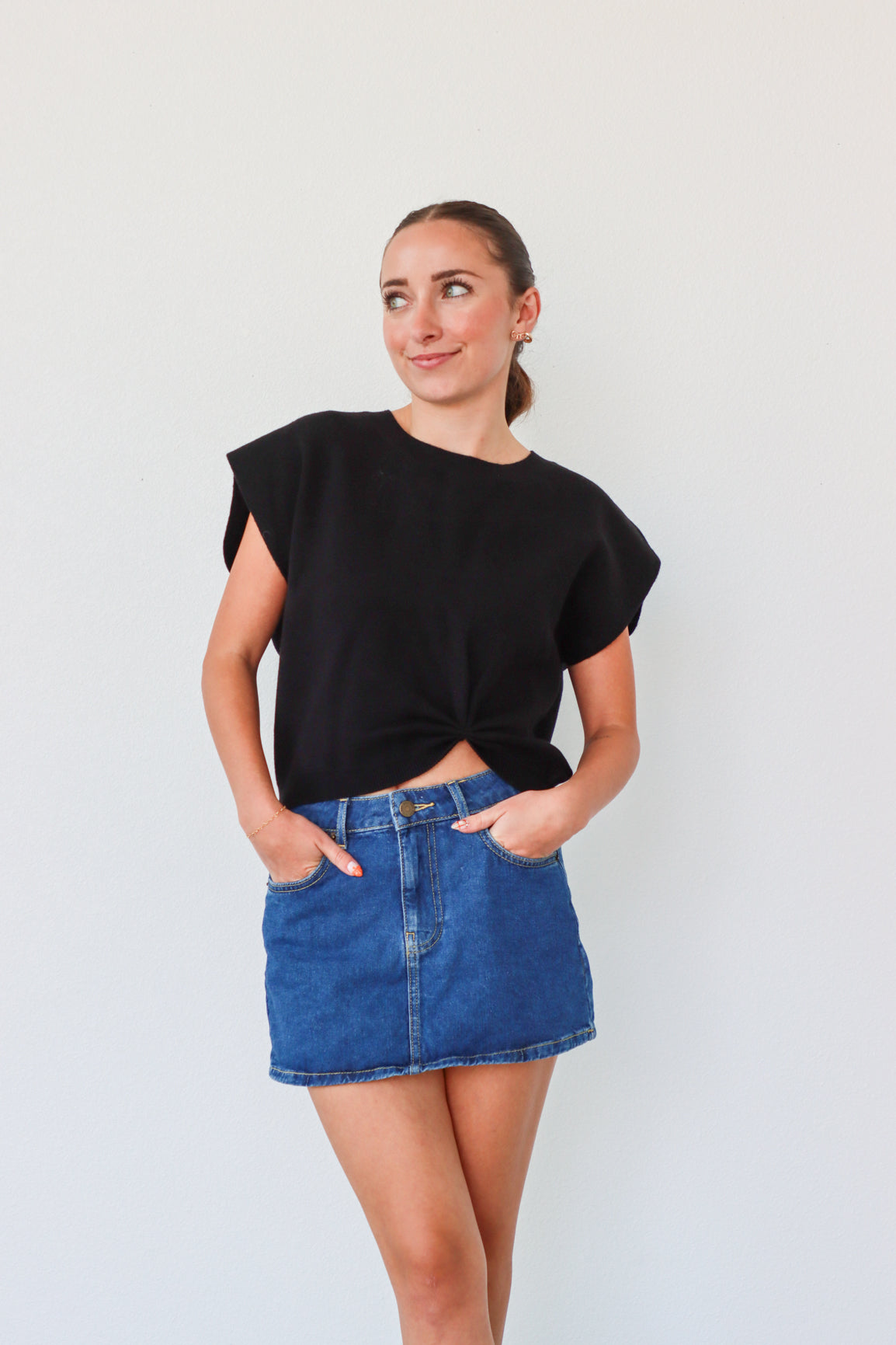 Woman wearing a black top and blue denim skirt against a plain background