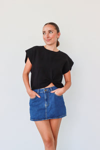 Woman wearing a black top and blue denim skirt against a plain background
