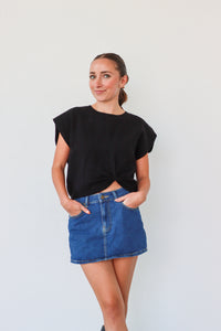 Woman wearing a black top and blue denim skirt against a white background