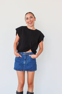 Woman wearing a black top and blue denim skirt against a plain background
