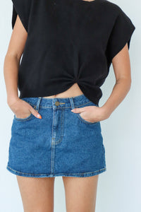 Person wearing a black top and blue denim skirt against a light gray background