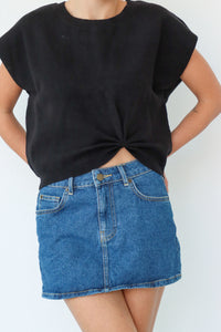 Person wearing a black t-shirt and blue denim skirt on a white background