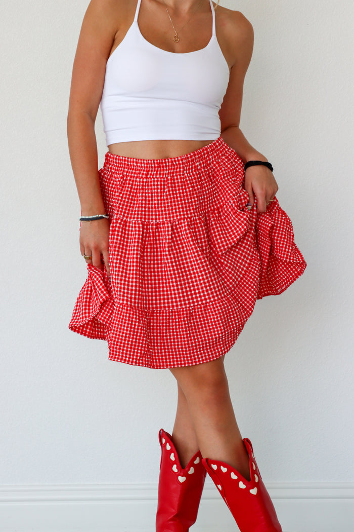 Person wearing a red checkered skirt and white top with red boots on a light background