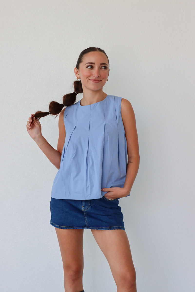 Woman wearing a light blue sleeveless top and denim shorts against a plain background