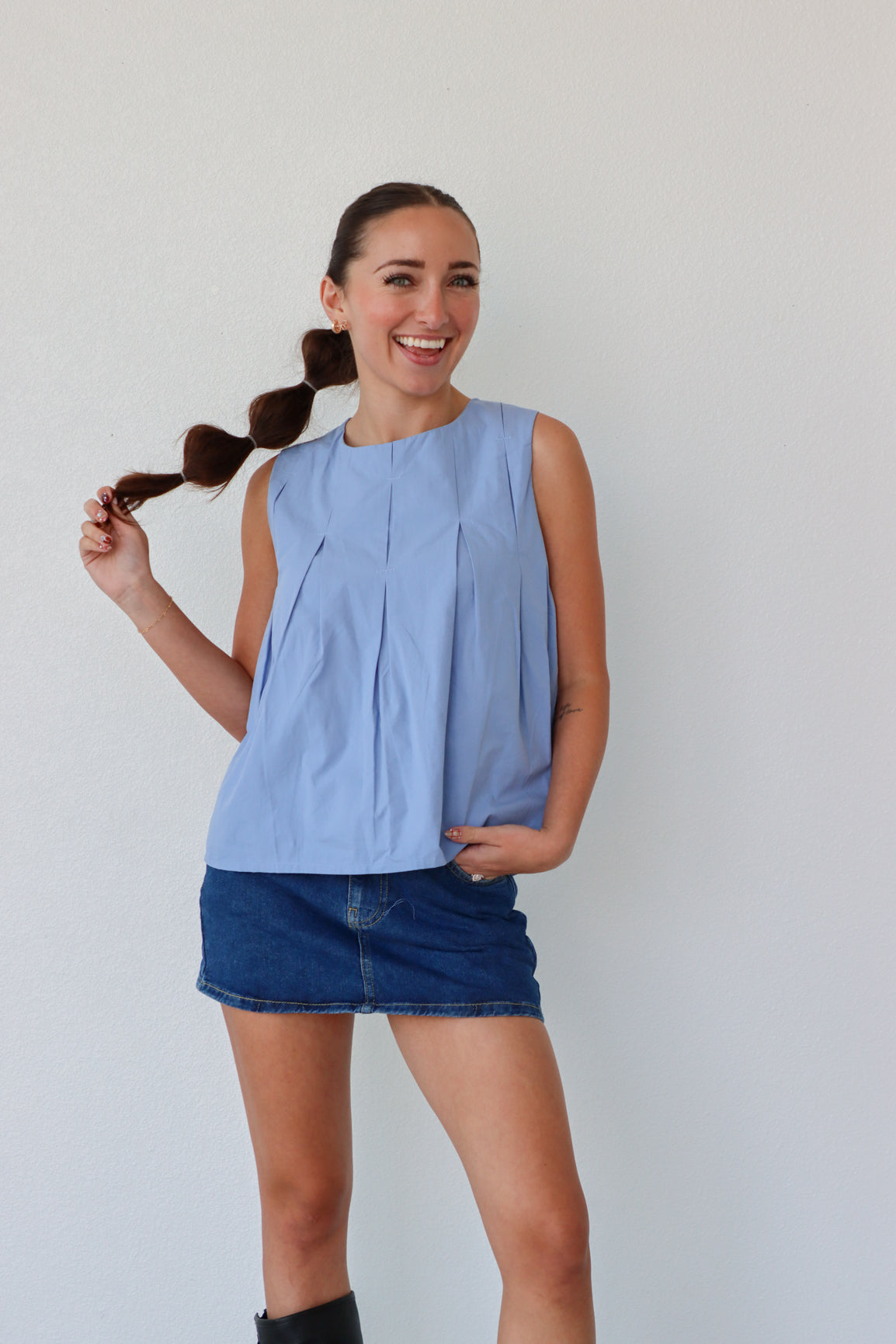 Woman wearing a light blue sleeveless top and denim shorts against a plain background