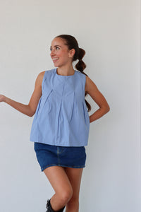 Woman wearing a light blue sleeveless top and denim shorts against a plain background