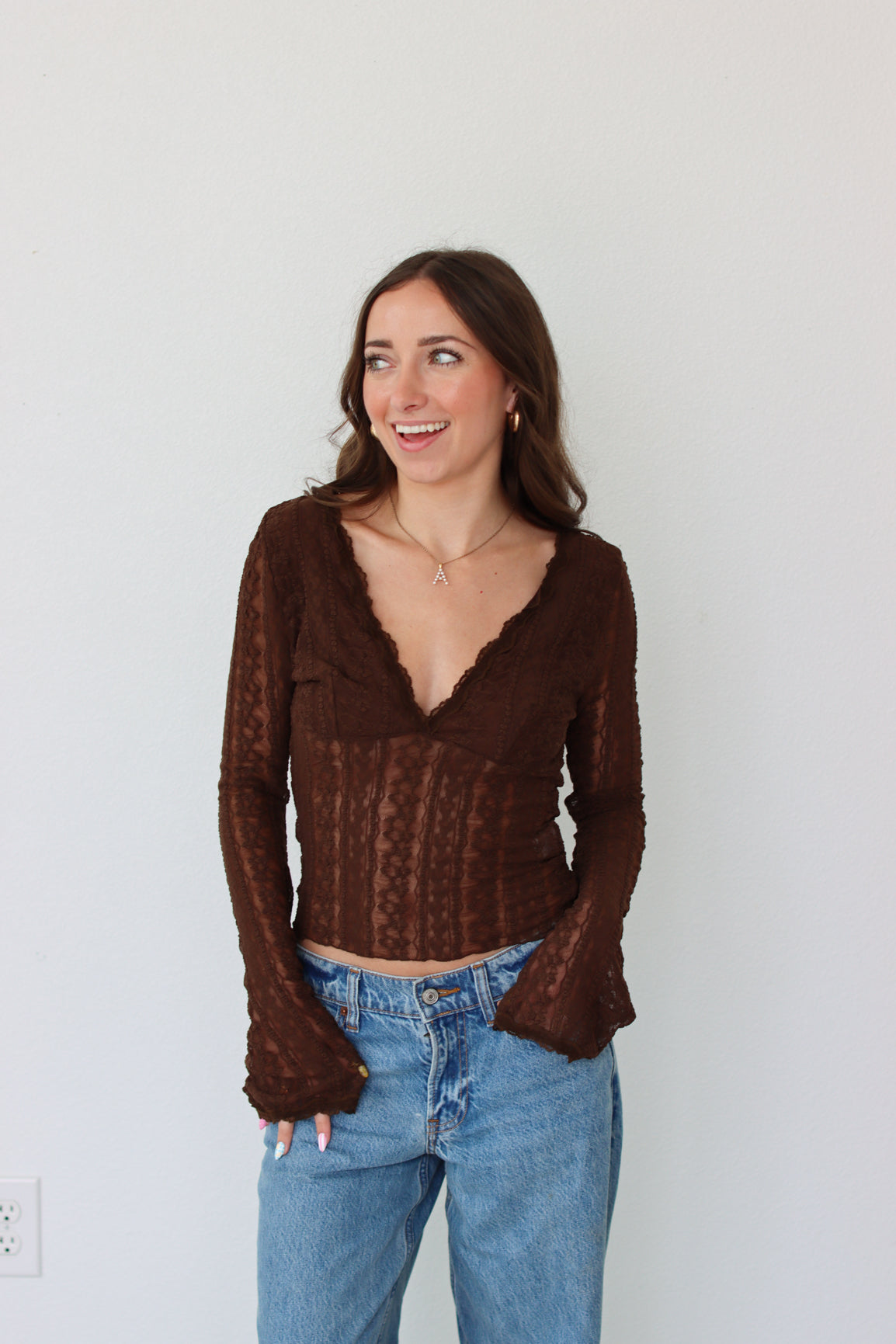 Woman wearing a brown mesh top and blue jeans against a white background