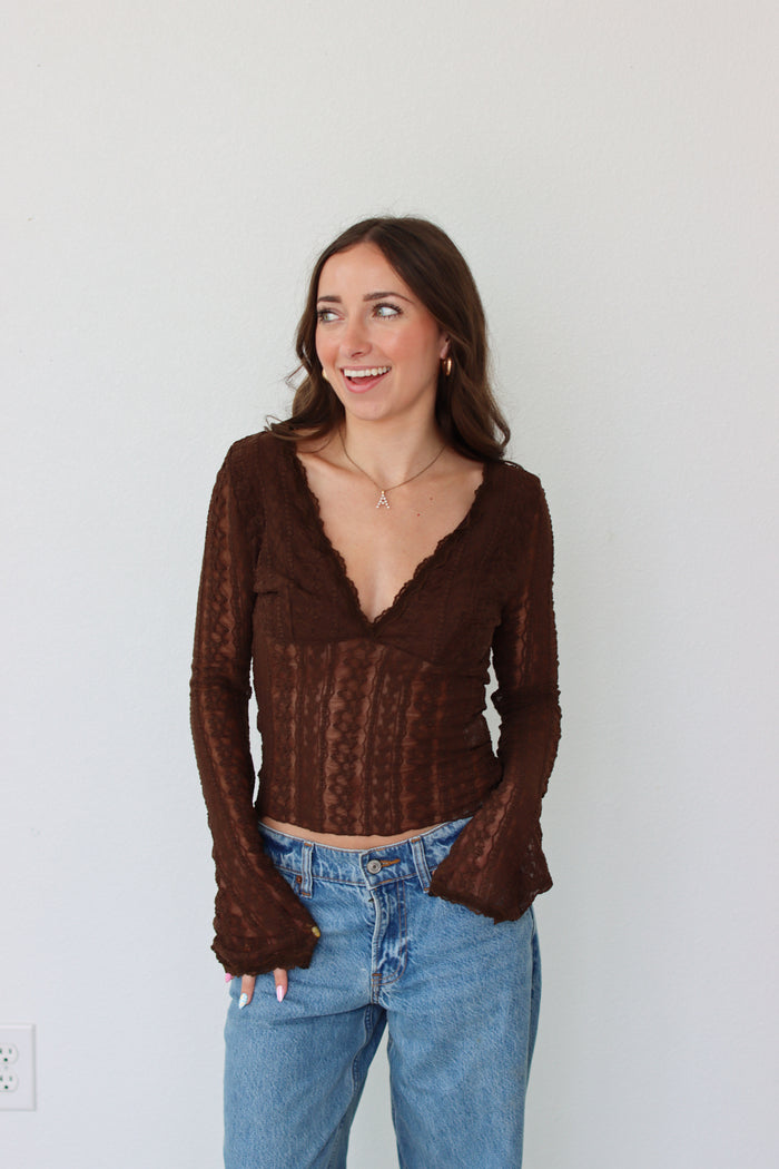 Woman wearing a brown mesh top and blue jeans against a white background