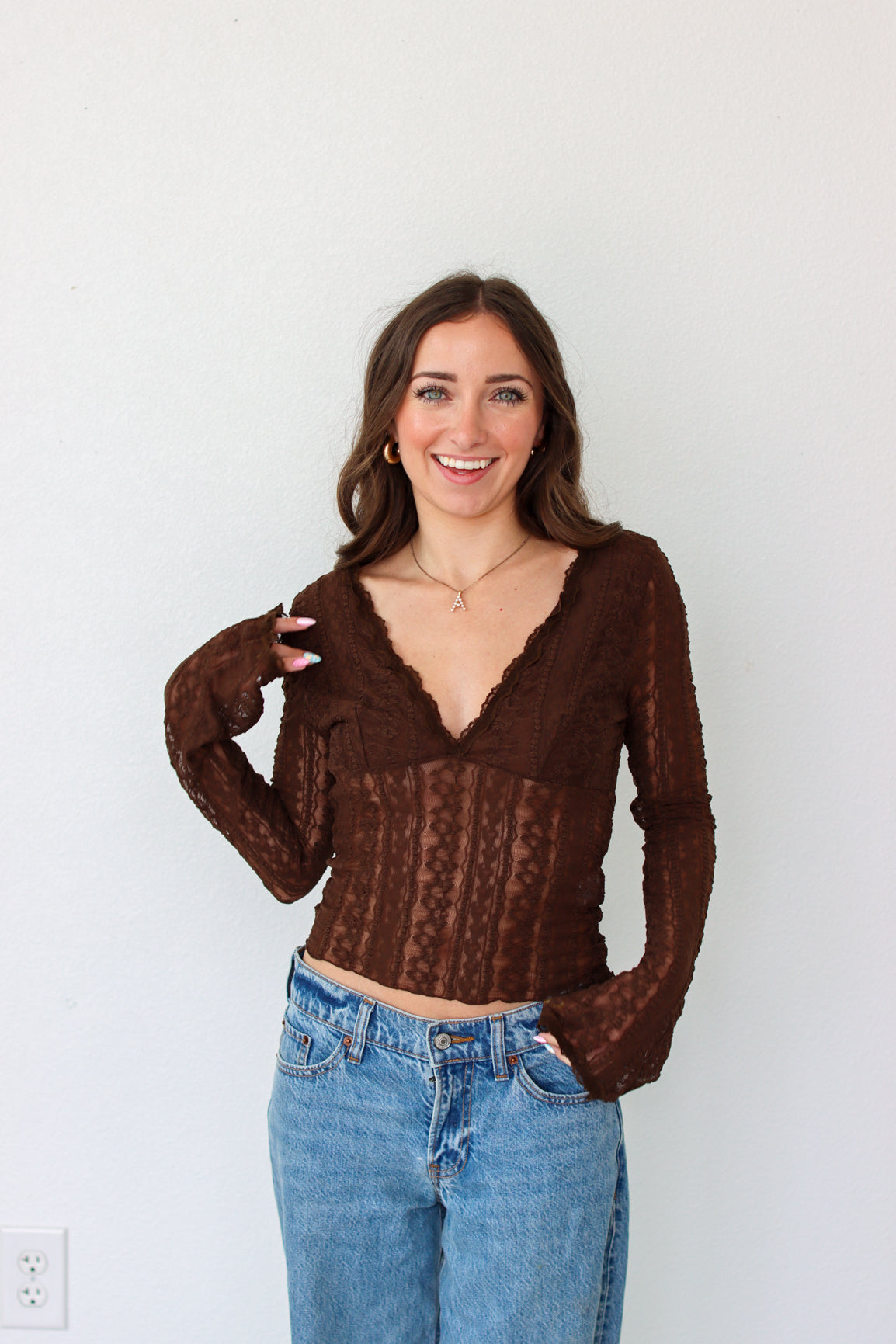 Woman wearing a brown mesh top and blue jeans against a white background