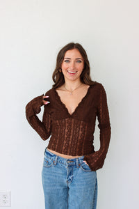 Woman wearing a brown mesh top and blue jeans against a white background