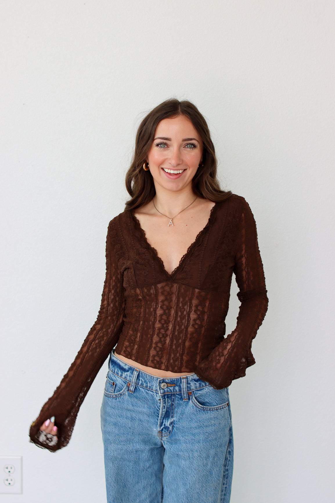 Woman wearing a brown mesh top and blue jeans against a white background