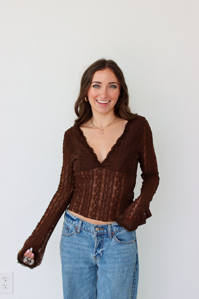 Woman wearing a brown mesh top and blue jeans against a white background
