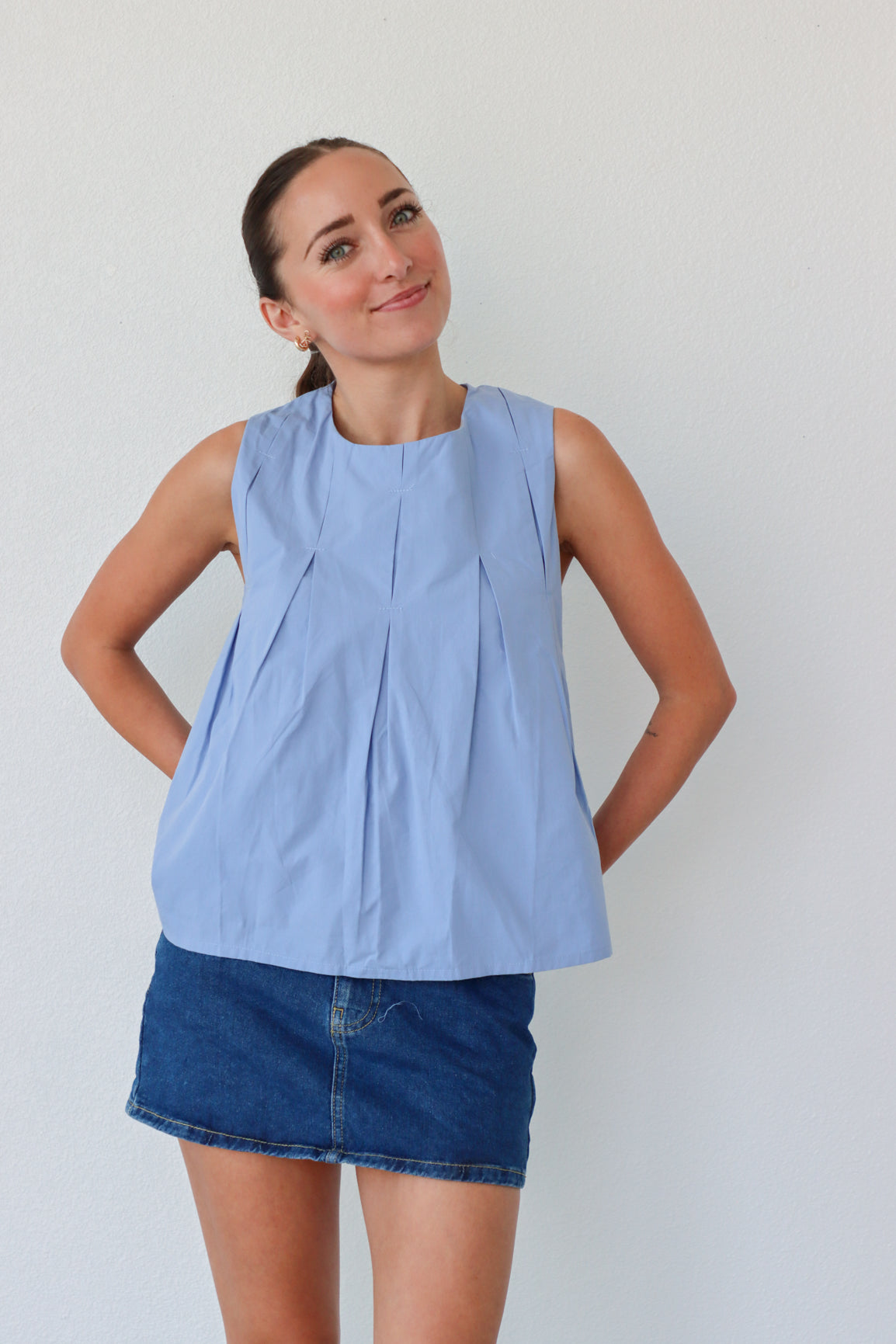 Woman wearing a light blue sleeveless top and denim skirt against a plain background