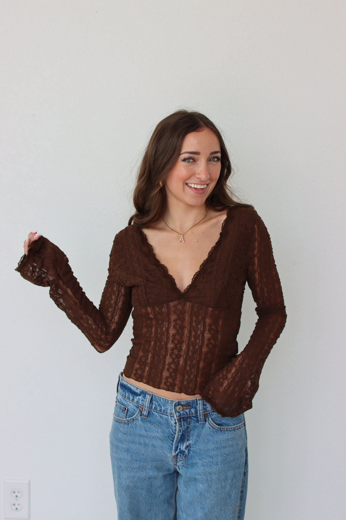 Woman wearing a brown mesh top and blue jeans against a white background