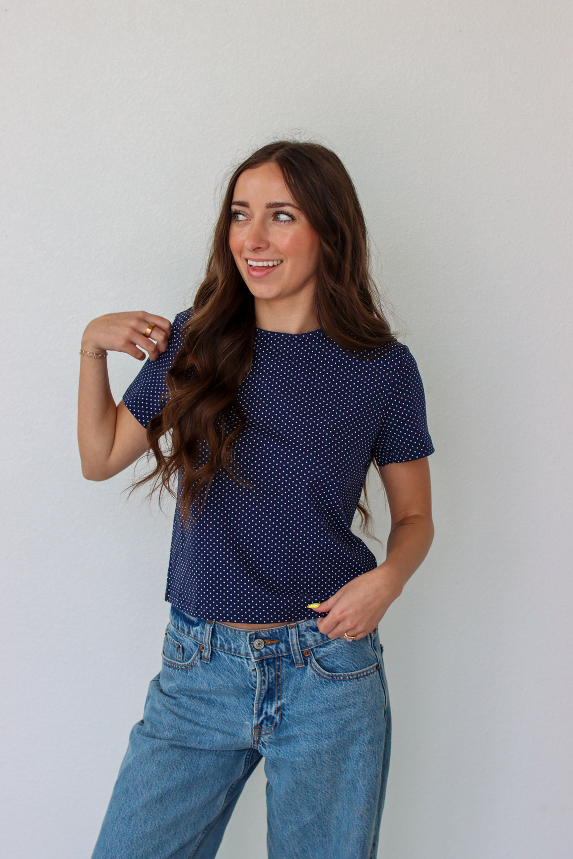 Woman wearing a blue polka dot shirt and jeans against a white background