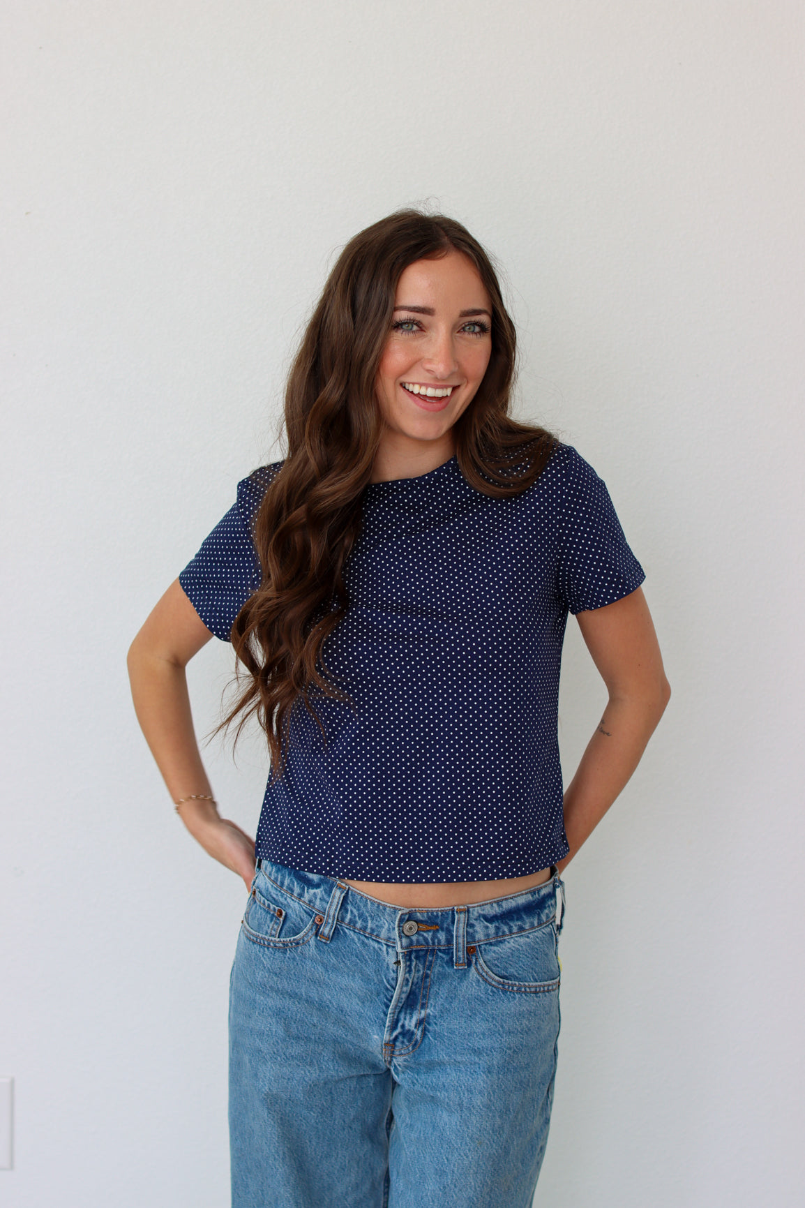 Woman wearing a navy blue polka dot shirt and blue jeans against a white background