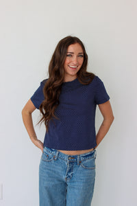 Woman wearing a navy blue polka dot shirt and blue jeans against a white background
