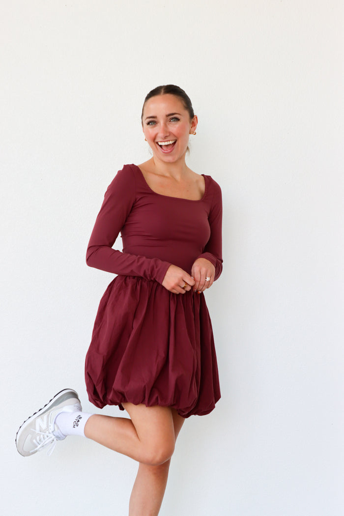 Woman wearing a burgundy dress with long sleeves on a white background