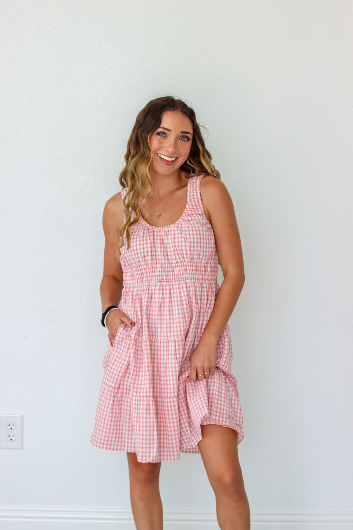 Woman wearing a pink checkered dress against a white wall