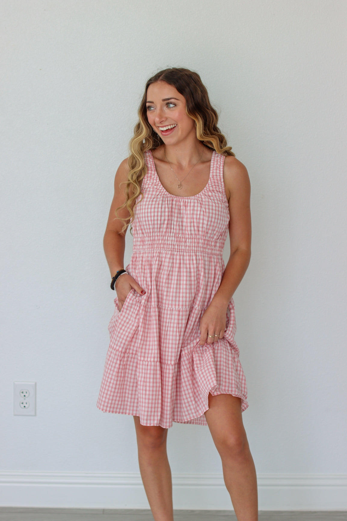 Woman wearing a pink checkered dress against a white wall