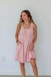Woman wearing a pink checkered dress against a white wall