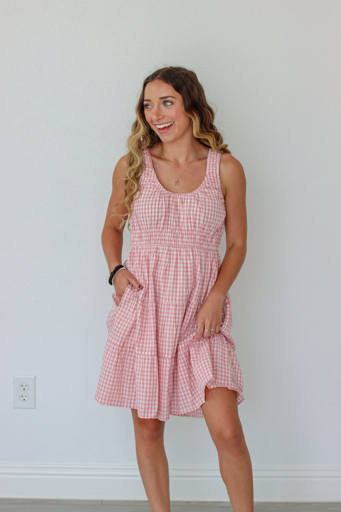 Woman wearing a pink checkered dress against a white wall