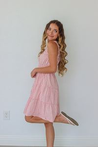 Woman wearing a pink checkered dress against a white wall