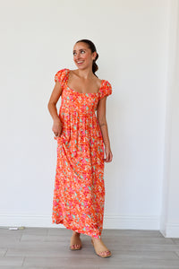 Woman wearing a floral dress standing against a white wall.