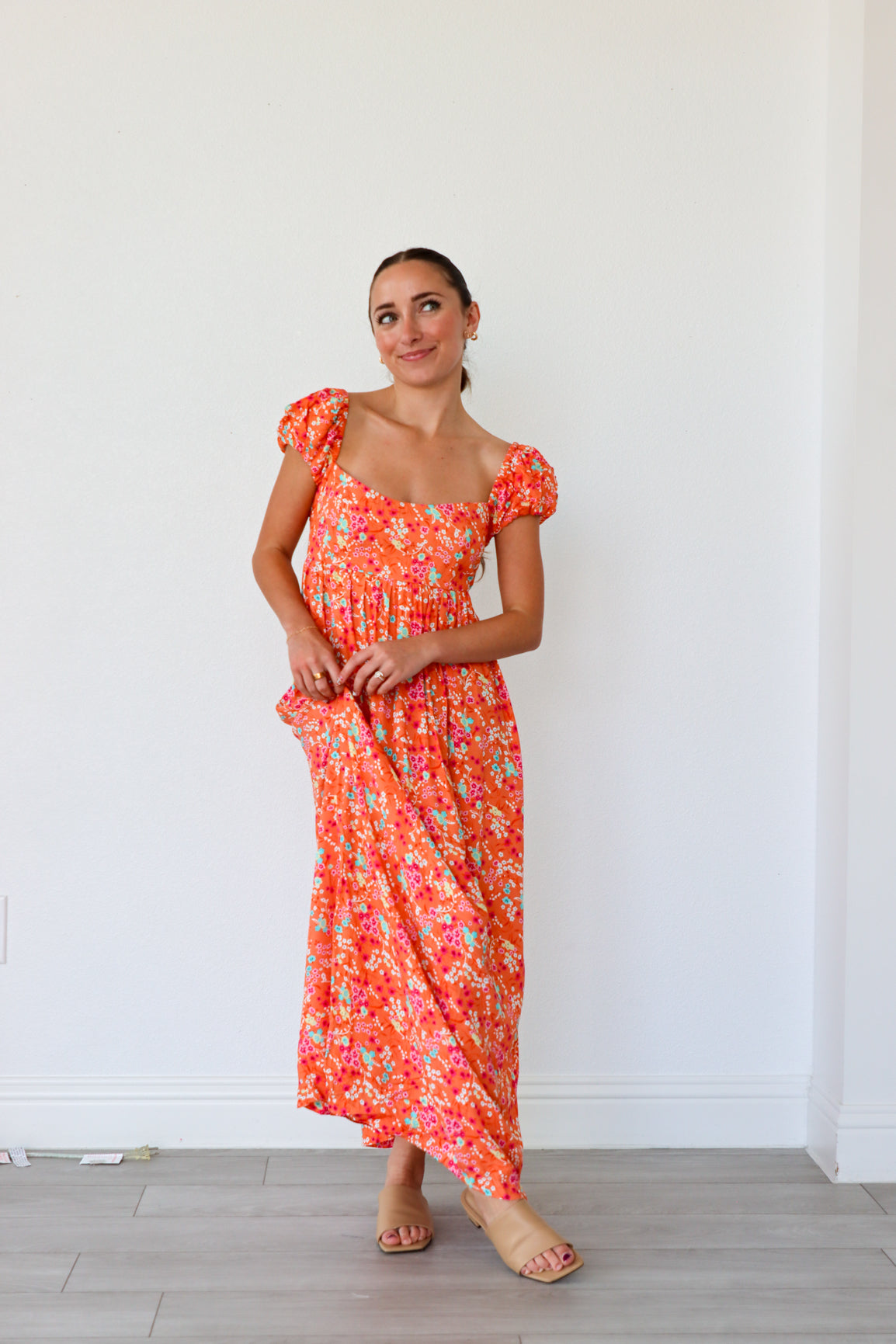Woman wearing a floral dress standing against a white wall.
