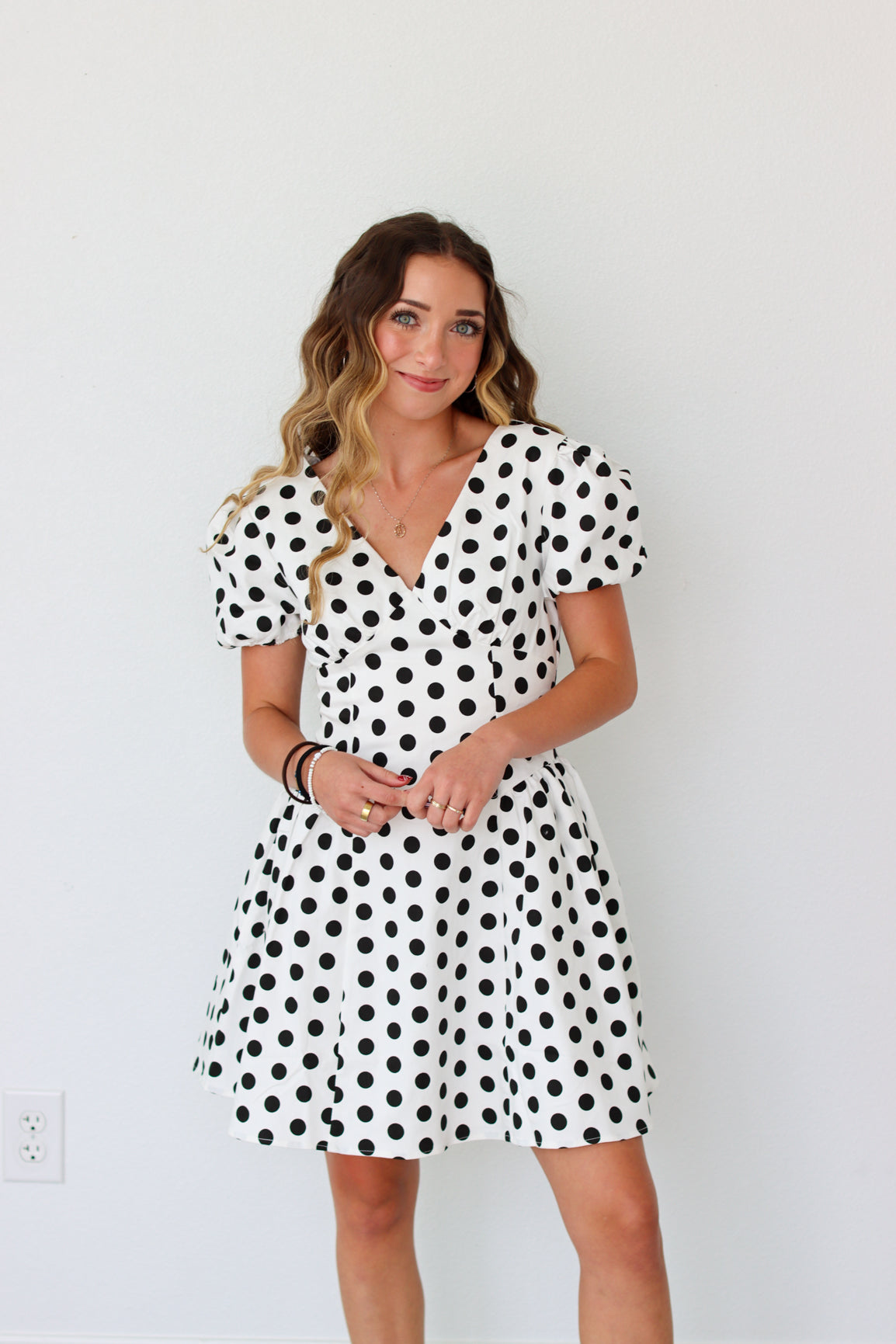Woman wearing a black and white polka dot dress against a plain background