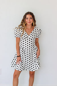 Woman wearing a black and white polka dot dress against a plain background