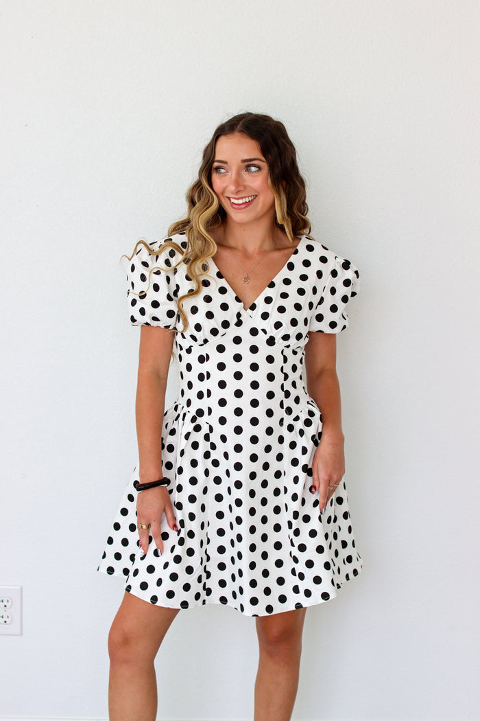 Woman wearing a black and white polka dot dress against a plain background