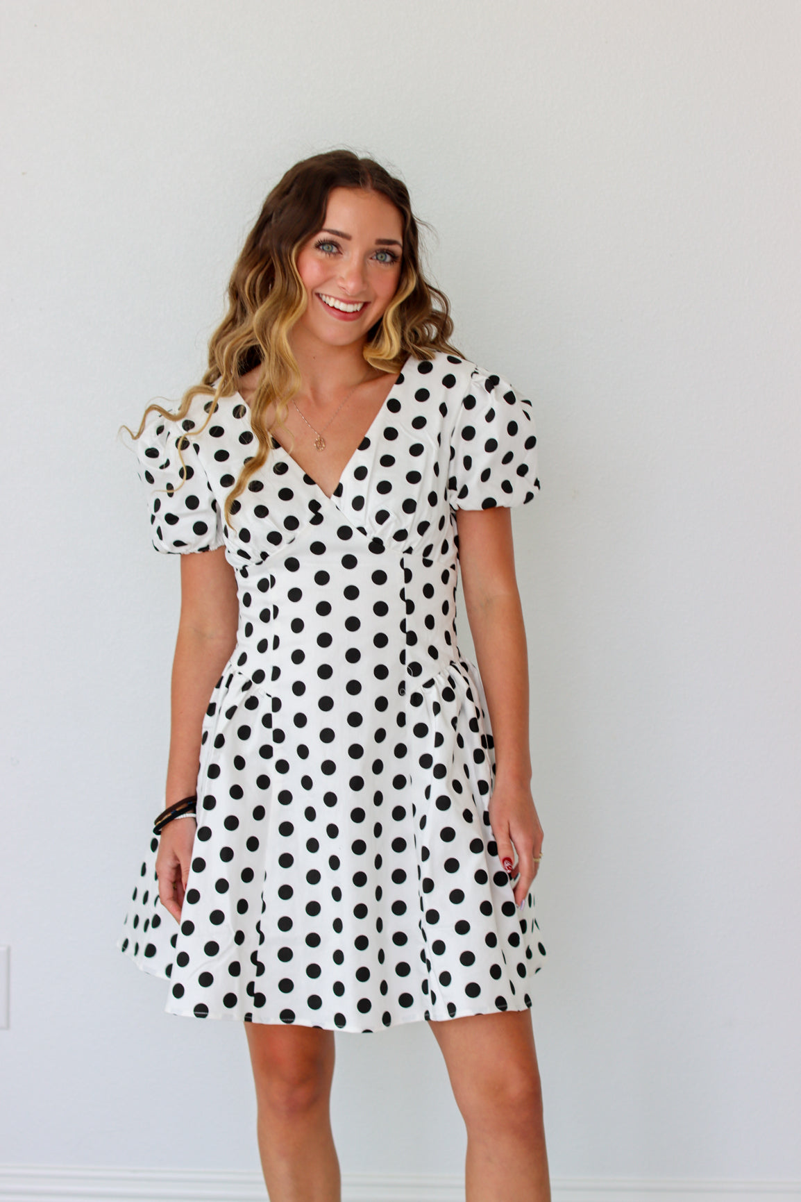Woman wearing a black and white polka dot dress against a plain background