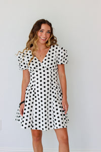 Woman wearing a black and white polka dot dress against a plain background